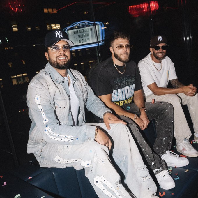 Three men wearing New York Yankees caps sit together in a dimly lit lounge area.