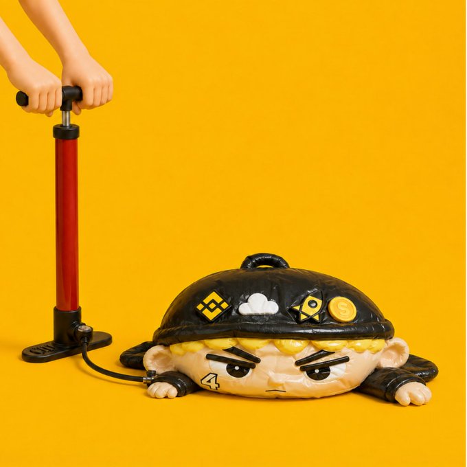A deflated inflatable mascot with an angry expression lies on the ground while hands pump air into it via a foot pump, set against a vibrant yellow background. The character features stickers including "4" on its cheek and symbols resembling crypto exchange logos (like Binance and others), symbolizing the need to recharge energy at the start of the week—just like the post's message of giving yourself a pep talk to kick off Monday with renewed motivation.