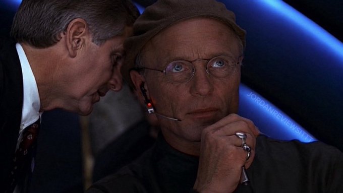 A scene from the movie 'Mars Attacks!' showing the characters Donald Kessler and Art Land whispering together, with a 'JORDANNEWS1' watermark visible.