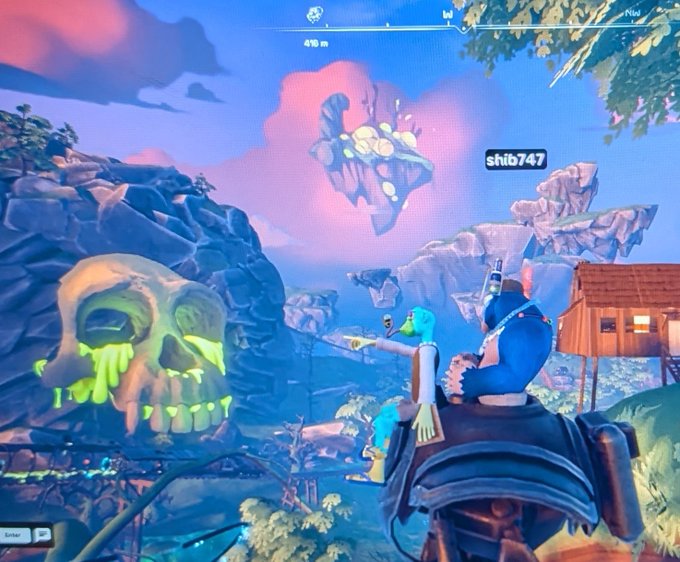 A screenshot from the video game Fortnite showing characters on a structure with a large skull rock formation and floating island in the background; player name 'shtb747' is visible.