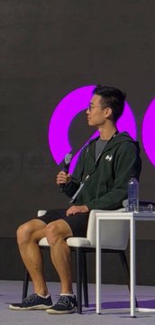 A young man is reclined in a chair holding a remote, appearing to be participating in some sort of presentation or discussion.