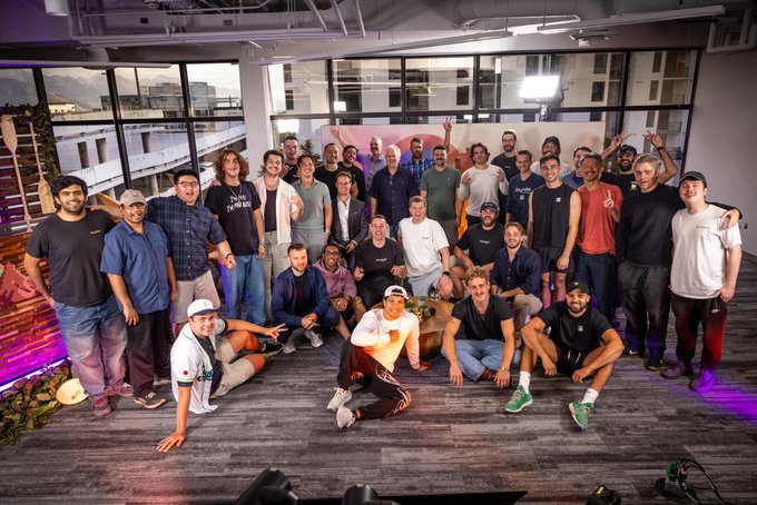 A large group of people posing for a team photo in what appears to be a modern office space with large windows.