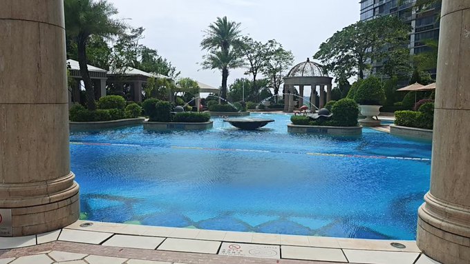 A luxurious outdoor pool area features a large blue pool surrounded by palm trees, a gazebo, and stone pillars.