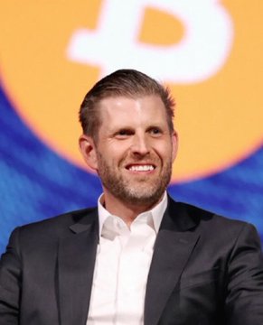 A smiling Eric Trump appears in front of an orange and blue backdrop, visually accompanying news that his company American Bitcoin ($ABTC) has expanded its treasury holdings to 8,300 BTC following a recent 300 BTC acquisition.