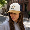 A woman wearing a white cap featuring a cartoon pigeon mascot, smiling on what appears to be a city street, tying into the "Pigeon Pizza Party" promotional post teasing a limited drop at 360.