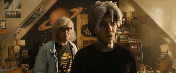 A scene from a movie showing two characters in a bedroom decorated with space-themed wallpaper; one is an older man wearing a 'Space Invaders' t-shirt.