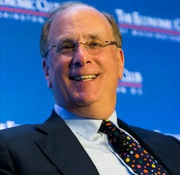 A man in a dark suit and patterned tie smiles while speaking at a podium, with a blue backdrop bearing 'The Business' and 'China' lettering behind him.