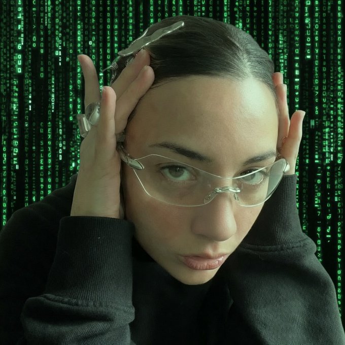 A woman in rimless glasses holding her head with both hands against a green Matrix-style digital code background.
