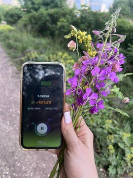 A hand holds a bouquet of purple wildflowers and a phone displaying a running workout screen showing a distance of 5.6 kilometers and a time of 29:50.