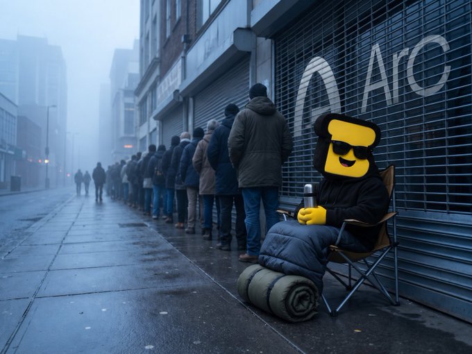 A line of people waits on a foggy city sidewalk near a storefront marked 'Arc,' while a person in a yellow mascot head and sunglasses sits in a camping chair with a thermos and sleeping bag.