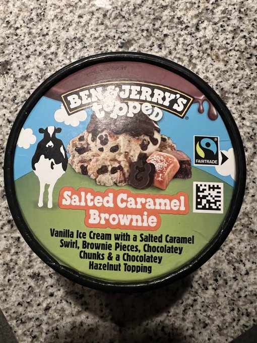 A top-down photograph of a Ben & Jerry's 'Topped' pint of 'Salted Caramel Brownie' ice cream resting on a speckled granite countertop, showing the Fairtrade logo and QR code on the lid.