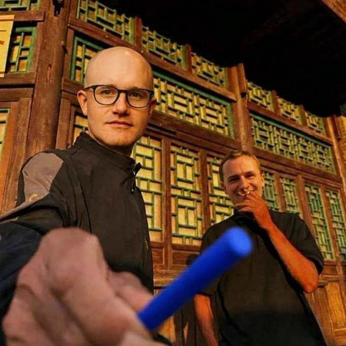 In this image, two men are shown in front of an ornate, traditional building, with one man holding a blue object that looks like a pen toward the camera. The image visually represents the concept of "posting" or creating content, which is central to the accompanying text about starting movements.