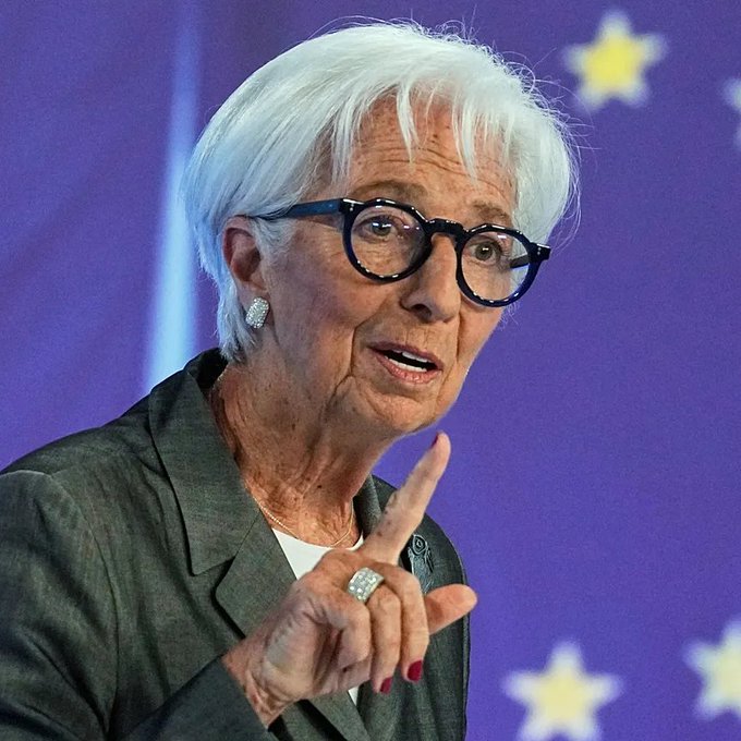 The image shows an older woman with short white hair and dark-rimmed glasses, wearing a gray blazer and gesturing with her finger while speaking, set against a blue background with yellow stars reminiscent of the EU flag. The accompanying post about Germany's sale of seized Bitcoin at a major loss relates to her likely role as a German or EU government official who would have been involved in such a financial decision.
