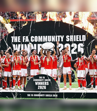 The Arsenal football team celebrates winning "THE FA COMMUNITY SHIELD WINNERS 2026" while lifting the trophy amid streamers and confetti.