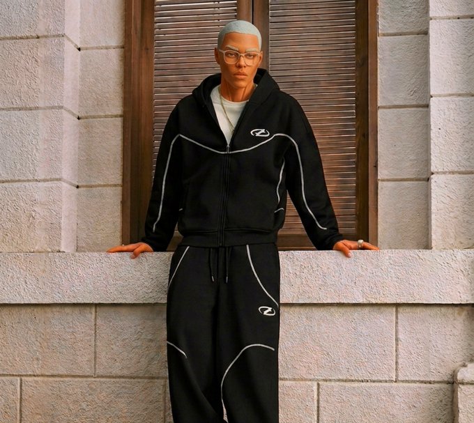 A person with short bleached hair and glasses wears a black zip-up tracksuit with white piping and matching sweatpants, leaning against a stone window ledge.