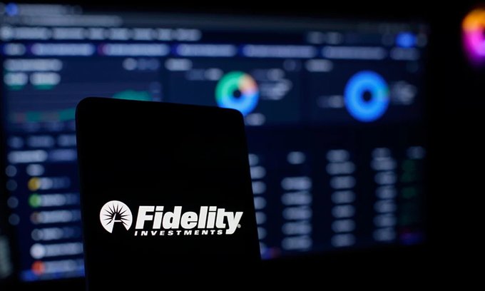 A smartphone displaying the illuminated 'Fidelity Investments' logo silhouetted against blurred stock market data screens in the background.