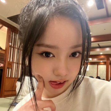 A close-up selfie of a young woman with dark hair posing indoors, resting her chin on her finger.