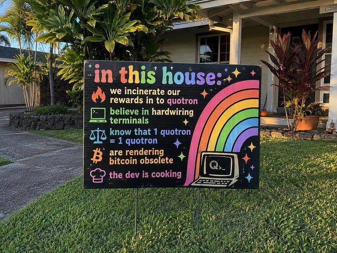 A yard sign in front of a house with text including 'in this house:', 'we incinerate our rewards in to quotron', 'believe in hardwiring terminals', 'know that 1 quotron = 1 quotron', 'are rendering bitcoin obsolete', and 'the dev is cooking'.