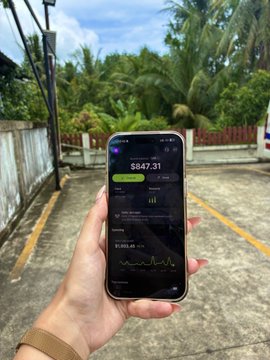 A hand holds a smartphone displaying the Jupiter Mobile (@jup_mobile) app interface with a portfolio value of $847.31, set against a tropical backdrop with palm trees. The image visually reinforces the post's theme of using Jupiter Mobile as an essential on-the-go tool for trading and managing crypto assets while traveling.