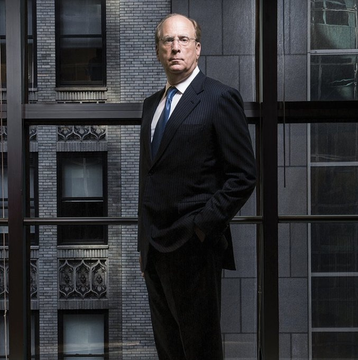 A man in a dark suit stands with hands in pockets in front of large windows overlooking a brick building, suggesting a corporate setting that ties to the post about BlackRock's involvement with Solana. The professional portrait visually reinforces the message about institutional crypto accumulation by BlackRock.