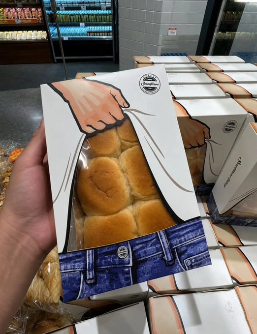 The caption: A hand holds a box labeled "StreetTeam" featuring a photo-realistic image of a hand pulling back paper to reveal brioche rolls, displayed near stacked boxes in a supermarket.

How it relates: The image riffs on the old "POV you're holding a bag of chips with a hand printed on it" meme, except here the packaging shows a hand "uncovering" the bread rather than baked-in chips — fitting the "Lmaoooo" reaction to this amusingly deadpan printed illusion.