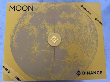 A gold and gray Binance-branded box labeled "MOON" featuring a detailed lunar surface design, presented as a Mid-Autumn Festival gift to celebrate the holiday. The moon imagery ties directly to the festival's traditional association with the full moon, while Binance branding suggests the gift came from a Binance employee or representative.