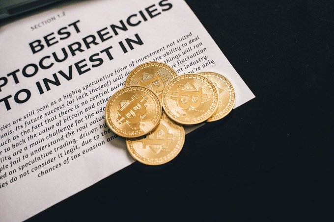 The image features a stack of gold Bitcoins, which are the main focus of the scene. The text "Best cryptocurrencies" can be seen next to these Bitcoins, indicating that they are being discussed or highlighted within this context. The rest of the image is black, making the Bitcoins stand out prominently against it.