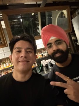 A selfie of two men in what appears to be a bar or restaurant, with one wearing a pink turban and the other smiling at the camera.