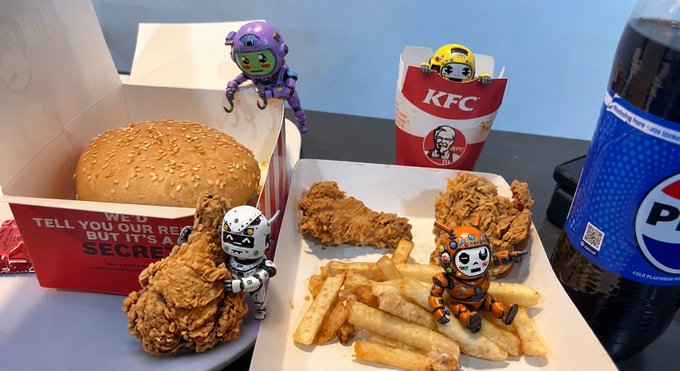 KFC meal (burger, fried chicken, fries, Pepsi) with a KFC paper bag, photographed with added Funko-style figurines around the food.