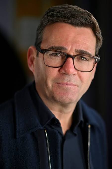 A middle-aged man with glasses and dark hair, wearing a navy jacket, poses for a portrait against a blurred dark background. The image accompanies news that Andy Burnham, who previously championed making Manchester a "Web3 powerhouse," may become the UK's next pro-crypto Prime Minister.