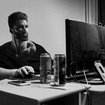 A black and white photo of a muscular bearded man intensely focused on a computer screen while using a mouse. Two beverage cans sit on the desk beside his monitor.