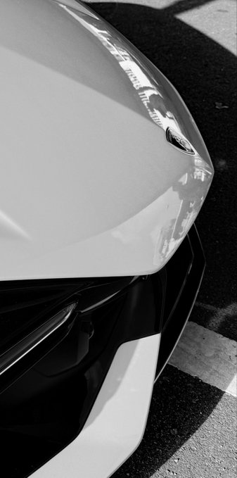 A close-up black-and-white shot of a sleek Lamborghini's front fender and headlight, emphasizing the luxury sports car that the post references as a symbol of financial success—contrasted with the tongue-in-cheek advice to focus on researching tokens like "Stonk Brockers" rather than "degenerate activities."
