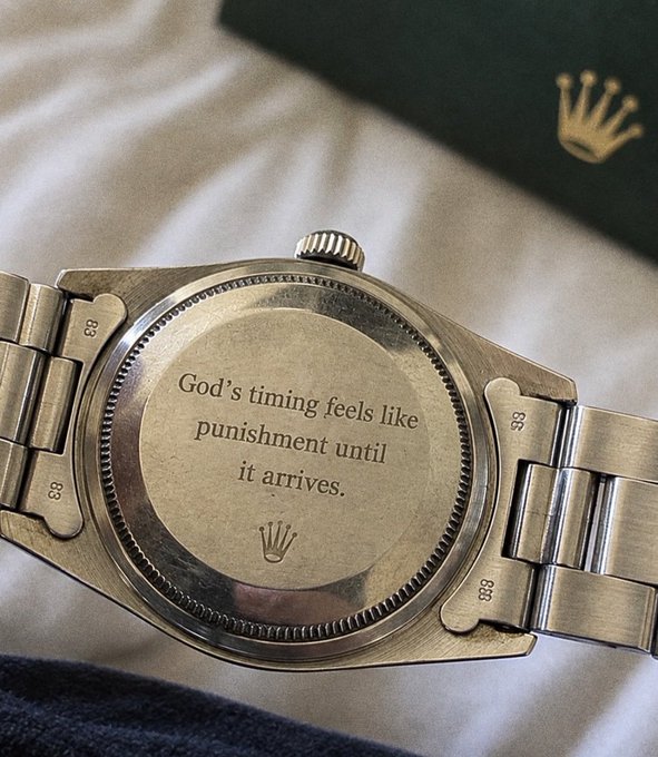 The back of a vintage Rolex watch featuring the engraved quote 'God's timing feels like punishment until it arrives.' alongside the Rolex crown logo, with a green Rolex box visible in the background.