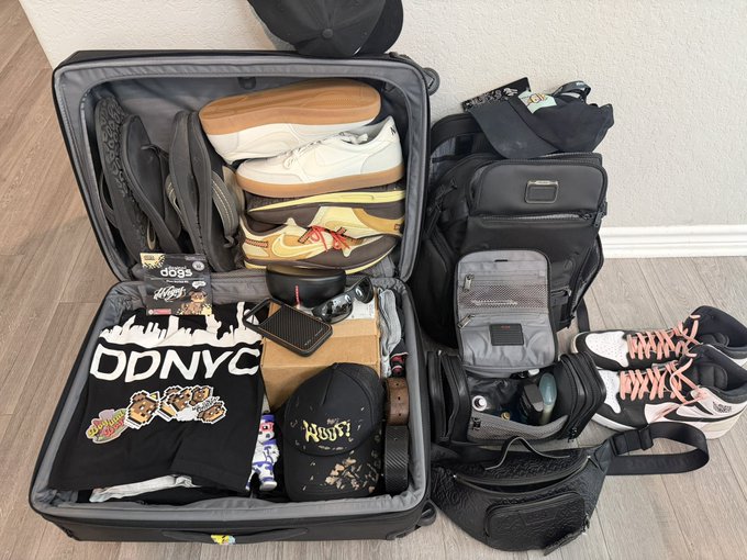 A suitcase packed for the upcoming "DDNYC" trip features a t-shirt, several pairs of sneakers (including Air Jordan 1 Lows and what appear to be Travis Scott or similar designer sneakers), a backpack, a cap labeled "MISFITS," and Doginal Dogs accessories. The image directly illustrates the post's excitement and preparation for the "DDNYC" event, showing items geared for the dog-themed community gathering.