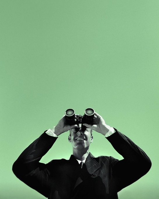 A sharply dressed man in a black suit holds binoculars to his eyes, gazing upward against a vibrant green background with a confident smile.

The image evokes the sense of an investor scanning the horizon for the next big opportunity, mirroring the post's theme of "conviction" as a guiding force in crypto—watching market trends and staying ahead of the crowd's sudden shifts between utility-driven projects and meme trading.