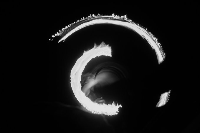 A high-contrast black and white abstract image showing a bright, swirling white shape resembling a stylized letter or flame against a dark background.