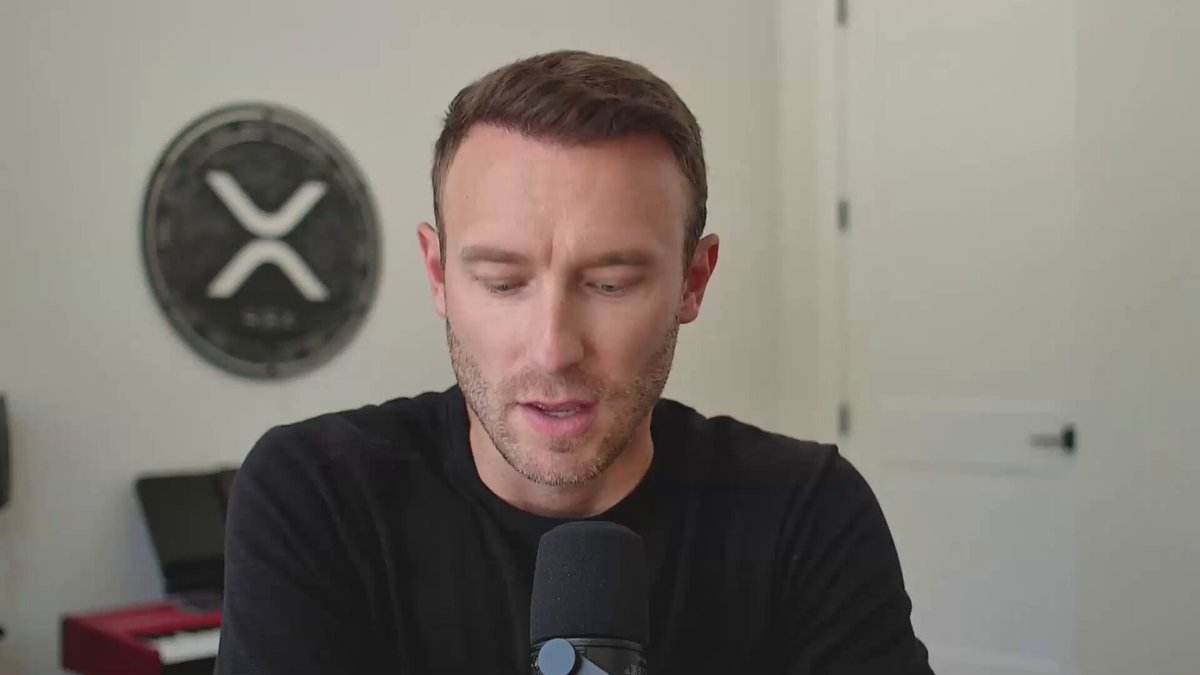 A man wearing a black shirt is talking into a microphone while sitting at a desk. He appears to be speaking about XRP, worth $95 million. The image includes text that says "XRP WEALTH TRANSFER - Being Worth $95 Million And The Mistakes I Made TradeConfident.io". This could imply that the man is discussing his experiences and lessons learned related to the XRP investment or wealth transfer process, with a focus on some of the mistakes he made during this venture in his words.