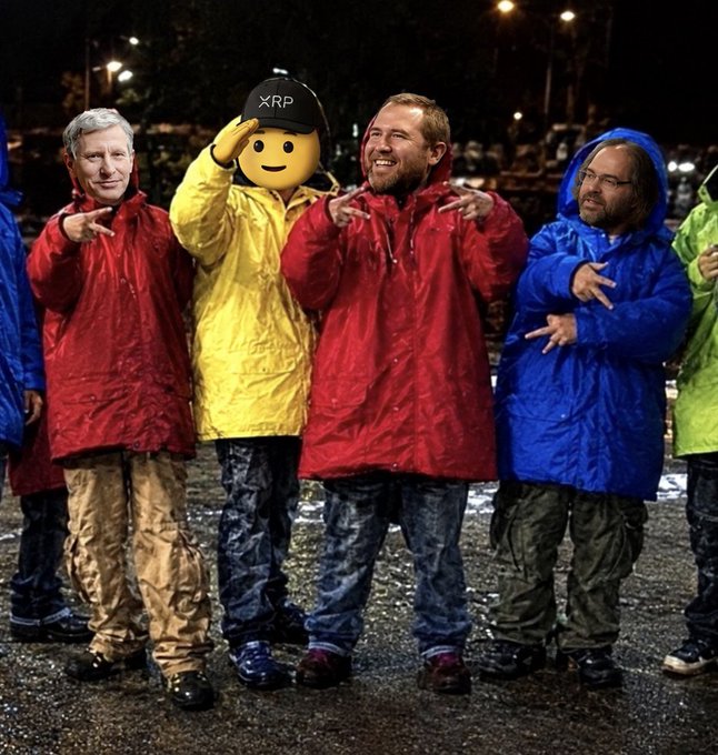 Four people in red, yellow, and blue rain ponchos pose at night in a parking lot, including one wearing an XRP hat, with their hands making gestures.