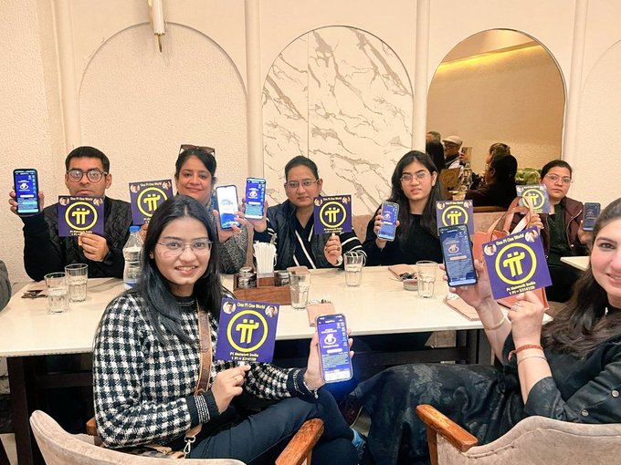 Group of people at a table holding up purple Pi Network cards and smartphones displaying Pi Network apps.