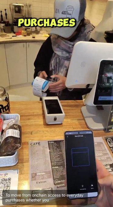 A screenshot from a video showing a person at a cafe counter using a payment terminal, with another person scanning a QR code on their phone to make a purchase, captioned 'To move from onchain access to everyday purchases whether you'.