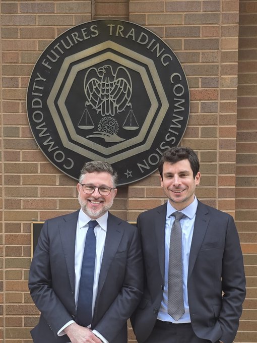 Two men in dark suits smile as they pose in front of the "Commodity Futures Trading Commission" (CFTC) seal mounted on a brick wall, with the post indicating they are Grayscale CEO Peter Mintzberg and CLO Craig Salm during their visit to Washington, D.C. for the CFTC's Innovation Advisory Committee meeting on digital assets.