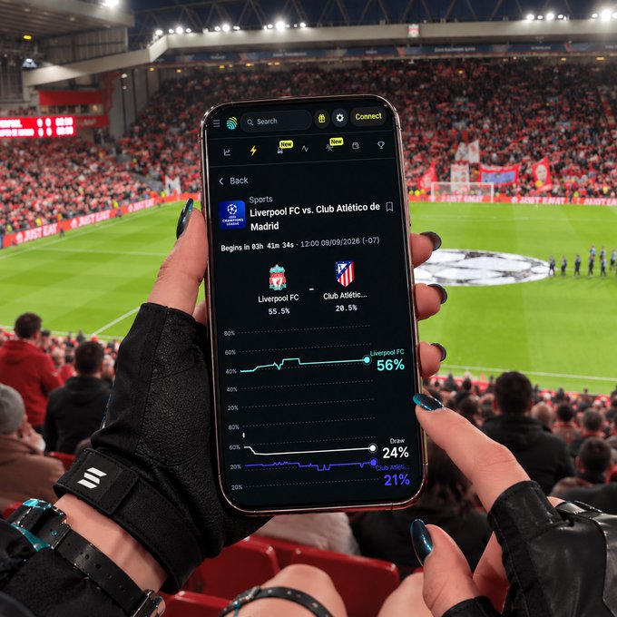 A fan holds up a smartphone at a packed stadium, displaying live betting odds for the Liverpool FC vs. Club Atlético de Madrid Champions League match, with Liverpool FC shown at 56% to win against Atlético's 21%. The odds chart and "JUST EAT" stadium signage capture the electric atmosphere as supporters back their team in the highly anticipated fixture.