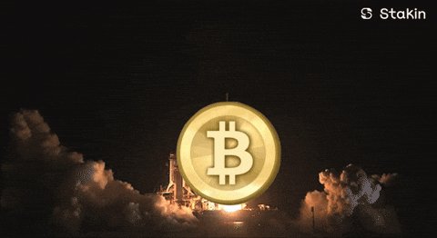The image features a coin that says "Bitcoin" on it along with a small rocket on top of it. There are two people in the image, one standing near the center while the other stands towards the right side. They appear to be looking at the coin and the rocket together. The caption below the image states that someone has asked, "Do you guys think the current Bitcoin price is okay to buy in?" This shows that the post is related to Bitcoin and its value or potential for growth.