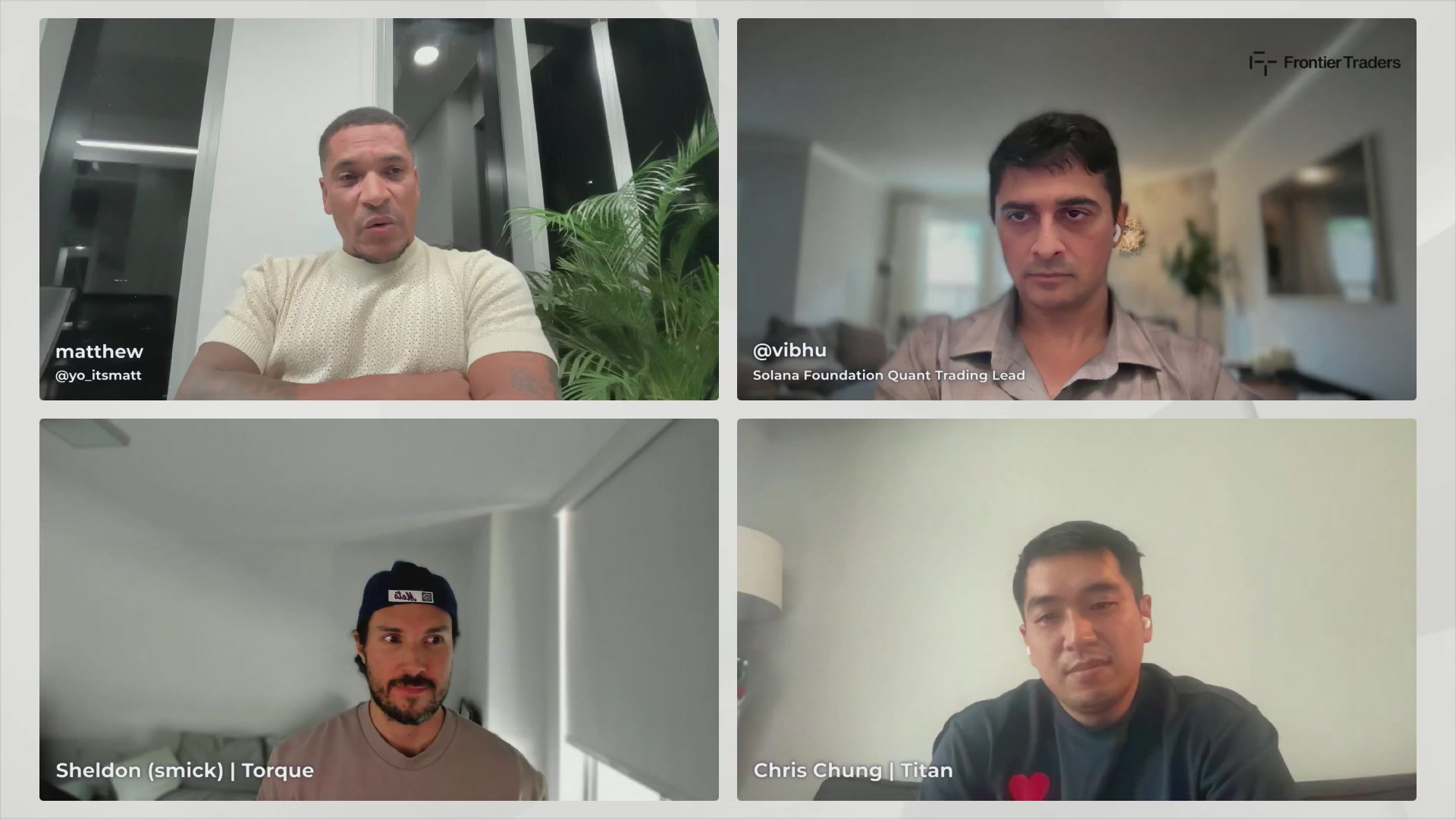 The image shows four men sitting at a table with their faces displayed on a computer screen. The first man has his arms crossed over his chest, while the other three are looking directly at the camera. They appear to be engaged in a video call or a group discussion. The background of the image is white and features a window that allows natural light into the room.