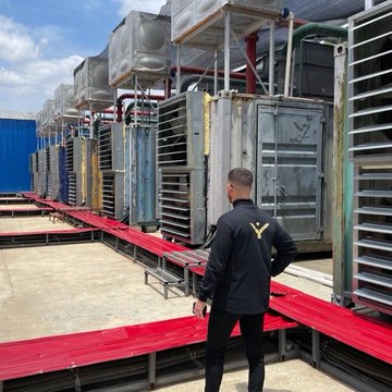 A worker in black uniform stands among rows of large industrial cooling units on a rooftop.