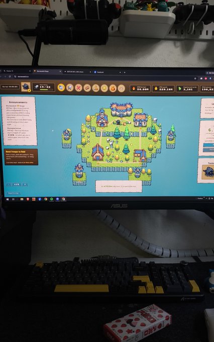 A computer monitor displays a pixel-art video game featuring floating islands with a small village, with a mechanical keyboard visible in the foreground.