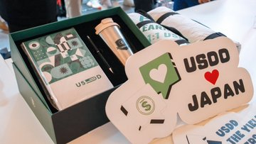 A box of USDD-branded merchandise and a decorative sign reading "USDD ❤ JAPAN" are displayed at the WebX Tokyo 2026 booth, highlighting the stablecoin's presence at the event.