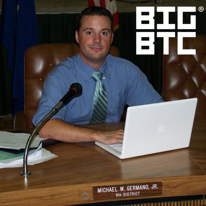 A man identified as 'MICHAEL W. GERMANO, JR., 8th District' sits at a desk with a microphone and laptop, with a 'BIG BTC' logo in the corner.