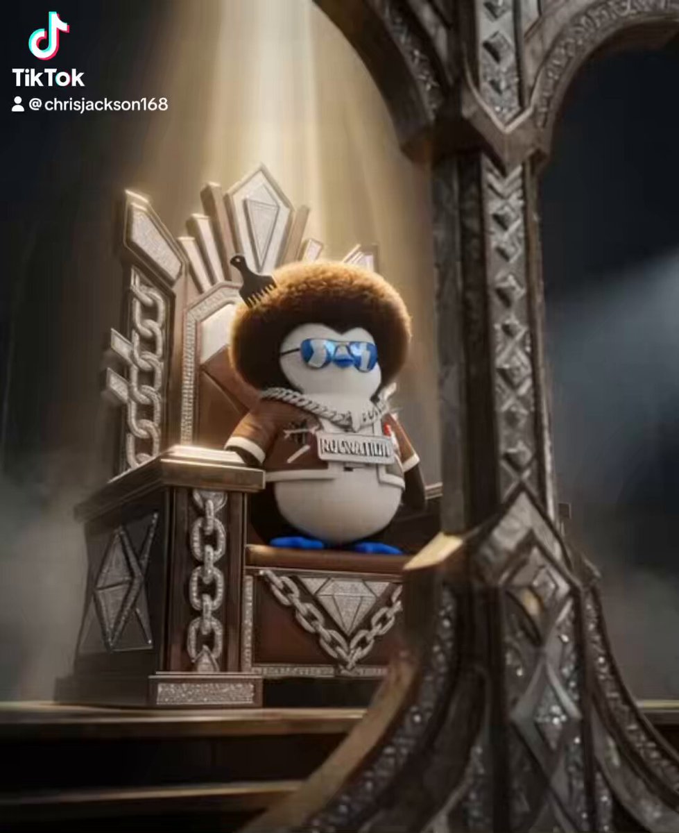 In the image, there is a cartoon penguin sitting on a chair with a crown on its head. The penguin has a brown fur coat and blue glasses. The background of the image features a dark room with a large mirror hanging above the penguin's head. The caption to the image reads "The Power Of $PENGU #Realz".