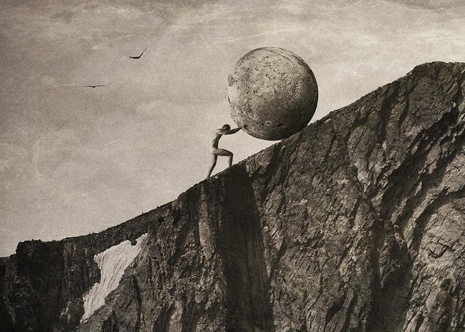 A surreal, sepia-toned image depicting a figure pushing a large stone sphere up a steep, rocky mountain cliff, with two birds flying in the cloudy sky.